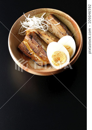 Overhead shot of thickly sliced char siu topped with white onion and boiled egg against a black background Overhead shot of thickly sliced char siu topped with white onion and boiled egg against a black background 109846592