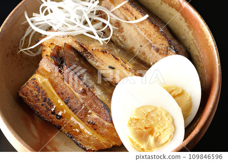 Overhead shot of thickly sliced char siu topped with white onion and boiled egg against a black background Overhead shot of thickly sliced char siu topped with white onion and boiled egg against a black background 109846596