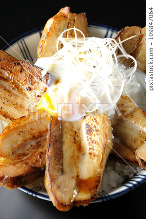 Overhead shot of thick-sliced char siu bowl topped with a soft-boiled egg against a black background 109847064