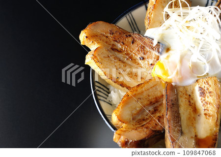 Overhead shot of thick-sliced char siu bowl topped with a soft-boiled egg against a black background 109847068