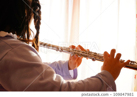 A girl in the fourth grade of elementary school is practicing the flute. 109847981