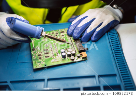 Electrician technician using hot soldering iron to fix repair small electrical digital computer circuit board fix repair with solder tin and lead 109852178