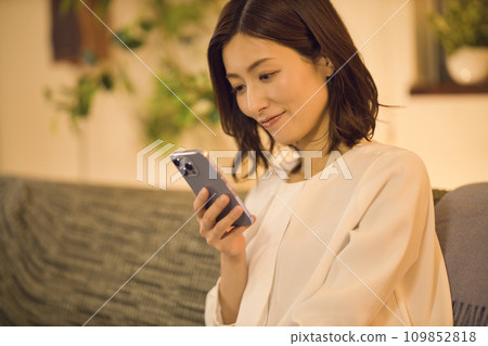 Night routine of a business woman who takes off her jacket and looks at her smartphone on the sofa Night routine of a business woman who takes off her jacket and looks at her smartphone on the sofa 109852818