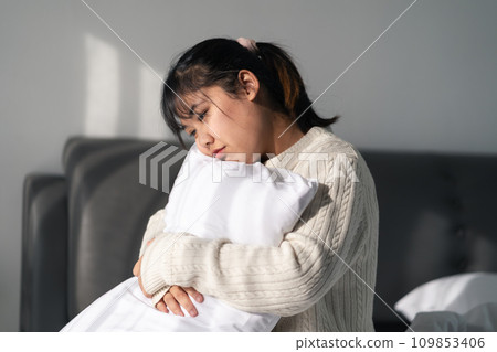 The sad and lonely woman is hugging a pillow on the bed in the bedroom at home. The sad and lonely woman is hugging a pillow on the bed in the bedroom at home. 109853406