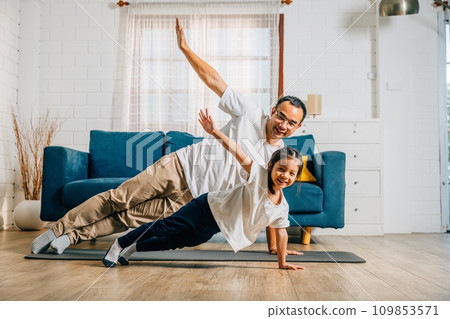 At home a father and his daughter enjoy a joyful yoga session focusing on togetherness happiness and muscle strength during their family fitness routine supporting each other. At home a father and his daughter enjoy a joyful yoga session focusing on togetherness happiness and muscle strength during their family fitness routine supporting each other. 109853571