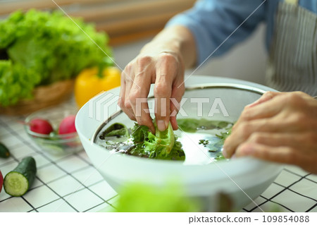 Hands of senior man sorting out fresh vegetables preparing a fresh healthy vegan salad in kitchen. Hands of senior man sorting out fresh vegetables preparing a fresh healthy vegan salad in kitchen. 109854088