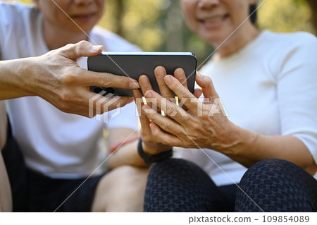 Happy senior couple resting and using mobile phone after morning workout. Happy senior couple resting and using mobile phone after morning workout. 109854089