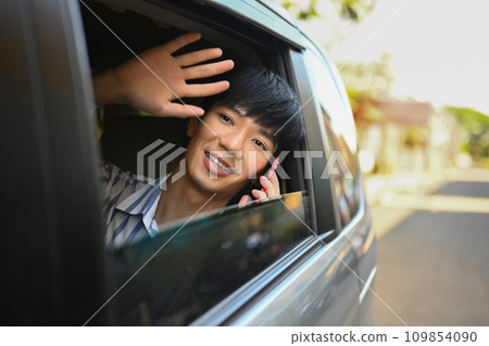 Happy man sitting in the car waving through the opened window. Transportation and vehicle concept concept. Happy man sitting in the car waving through the opened window. Transportation and vehicle concept concept. 109854090