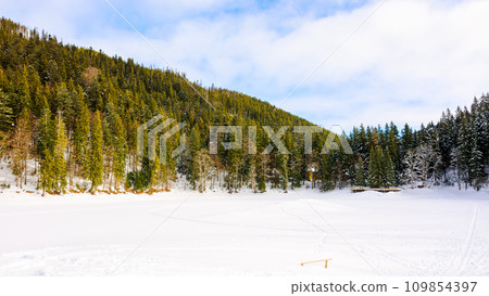 winter scenery with fir forest around the frozen snow covered lake. sunny weather with clouds on the sky 109854397