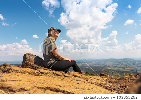 Tourist girl hiker resting at the top of the mountain and enjoying amazing landscape view of mountains and beautiful sky 109855262