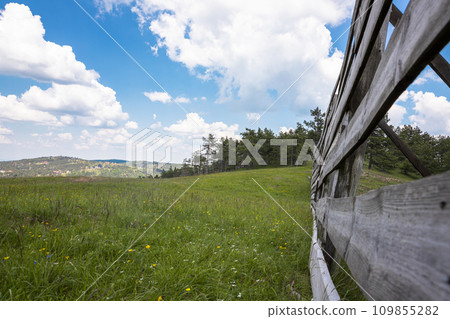 View of the wooden fence, meadow and amazing blue cloudy sky View of the wooden fence, meadow and amazing blue cloudy sky 109855282