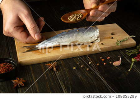The cook preparing Atlantic herring fish on the kitchen table with spices and coriander for a delicious lunch. Working environment on the kitchen table 109855289