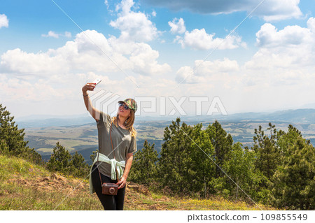 Tourist girl taking selfie with smartphone while Hiking in nature at the top of the mountain 109855549