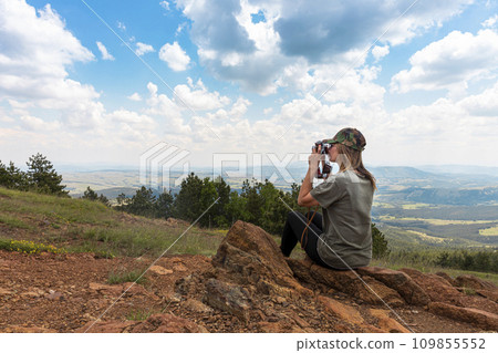 Tourist girl photographing with vintage photo camera at the top of the mountain peak Tourist girl photographing with vintage photo camera at the top of the mountain peak 109855552