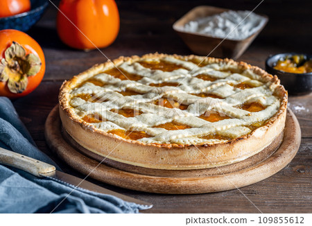 Italian homemade persimmon tart or crostata with ingredients on the wooden table, chiaroscuro 109855612