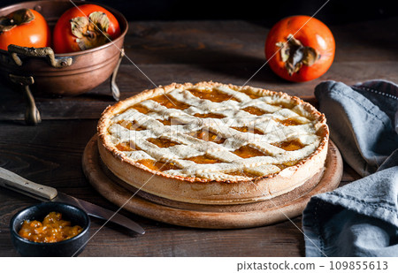 Italian homemade persimmon tart or crostata with ingredients on the wooden table, chiaroscuro 109855613