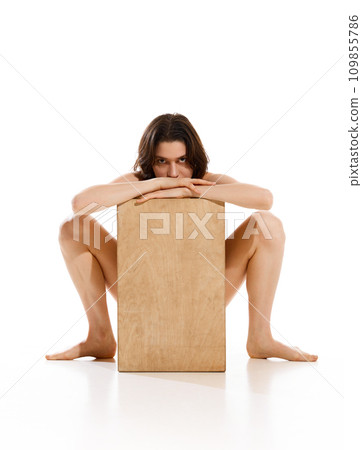 Creative full length portrait of slender naked young woman underwear posing sitting behind wood cube against white studio background. Creative full length portrait of slender naked young woman underwear posing sitting behind wood cube against white studio background. 109855786