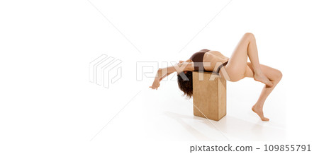 Captivating full length portrait of featuring young woman in brown underwear posing on wood cube against white studio background. 109855791
