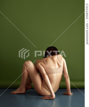 Rear view portrait of naked woman posing dressed beige lingerie sitting hugging legs on floor against olive studio background. Concept of natural beauty. Rear view portrait of naked woman posing dressed beige lingerie sitting hugging legs on floor against olive studio background. Concept of natural beauty. 109855913