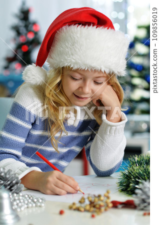 Happy girl in Santa hat sitting with Christmas present 109856019