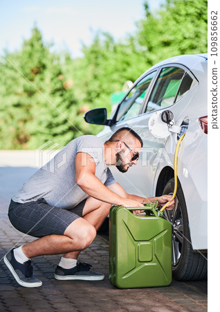Suspicious man stealing gasoline from car tunk. Thief trying to pump fuel from someone else's automobile. Stealing fuel in broad daylight. Suspicious man stealing gasoline from car tunk. Thief trying to pump fuel from someone else's automobile. Stealing fuel in broad daylight. 109856662