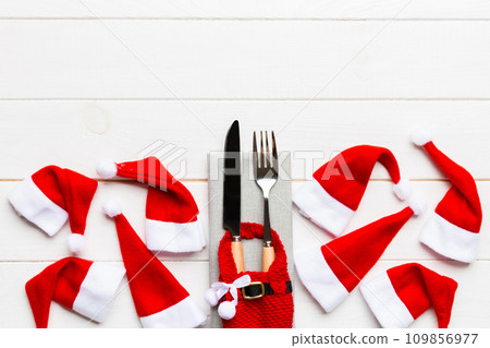 Festive set of fork and knife on wooden background. Top view of new year decorations and santa clothes and hat. Christmas concept with copy space 109856977