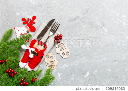 Top view of holiday objects on cement background. Utensils tied up with ribbon on napkin. Christmas decorations and reindeer with copy space. New year dinner concept Top view of holiday objects on cement background. Utensils tied up with ribbon on napkin. Christmas decorations and reindeer with copy space. New year dinner concept 109856983