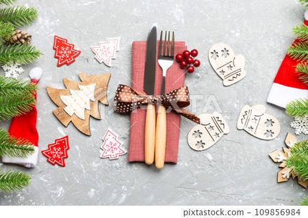 Top view of fork and knife on napkin with christmas decorations and new year tree on cement background. Close up of holiday and festive concept Top view of fork and knife on napkin with christmas decorations and new year tree on cement background. Close up of holiday and festive concept 109856984