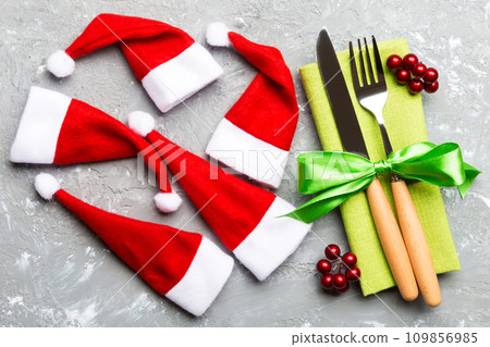 Festive set of fork and knife on cement background. Top view of new year decorations and santa clothes and hat. Close up of Christmas concept Festive set of fork and knife on cement background. Top view of new year decorations and santa clothes and hat. Close up of Christmas concept 109856985