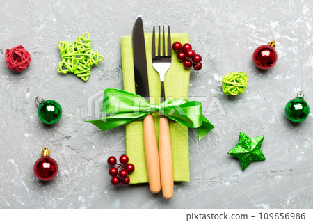 Top view of holiday set of fork and knife on cement background. Close up of Christmas decorations and toys. New Year Eve concept Top view of holiday set of fork and knife on cement background. Close up of Christmas decorations and toys. New Year Eve concept 109856986