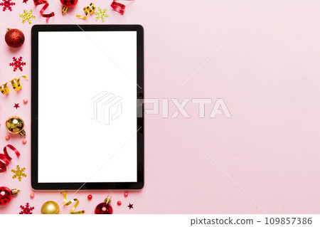 Christmas online shopping from home tablet pc with blank white display top view. Tablet with copy space on colored background with Christmas decorations balls,. Winter holidays sales background Christmas online shopping from home tablet pc with blank white display top view. Tablet with copy space on colored background with Christmas decorations balls,. Winter holidays sales background 109857386