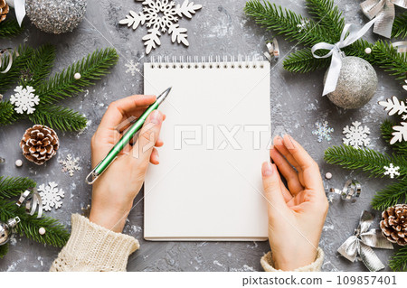 Woman writing Christmas to do list on notebook on colored background with xmas decorations Woman writing Christmas to do list on notebook on colored background with xmas decorations 109857401