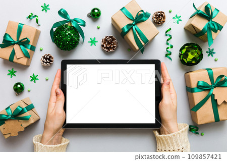 Christmas online shopping from home, female hands holding tablet pc with blank white display top view. woman hand holding tablet with blank screen, Christmas tree and gifts on background Christmas online shopping from home, female hands holding tablet pc with blank white display top view. woman hand holding tablet with blank screen, Christmas tree and gifts on background 109857421