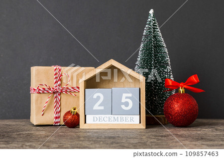 25 december. Christmas composition on colored background with a wooden calendar, with a gift box, toys, bauble copy space 109857463
