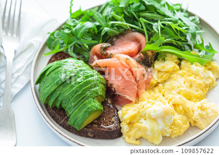 Keto breakfast - avocado toast, salmon, scrambled eggs and arugula, white background. 109857622