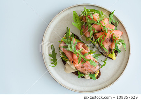 Rye toast with smoked salmon, avocado, hollandaise sauce and arugula. Rye toast with smoked salmon, avocado, hollandaise sauce and arugula. 109857629