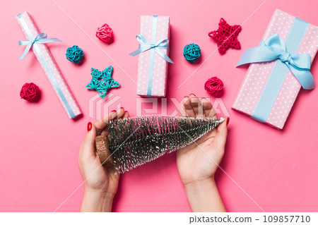 Top view of female hands holding christmas tree in her hand on pink background. New Year holiday concept. Mockup 109857710