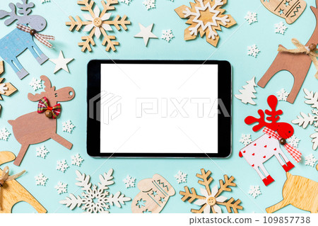 Top view of digital tablet on blue background made of holiday decorations and toys. Christmas ornament concept Top view of digital tablet on blue background made of holiday decorations and toys. Christmas ornament concept 109857738