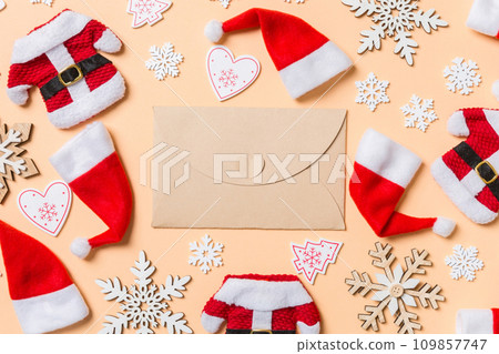 Top view of craft envelope with Christmas decorations and Santa hats on orange background. Happy holiday concept Top view of craft envelope with Christmas decorations and Santa hats on orange background. Happy holiday concept 109857747