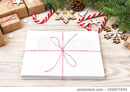 Envelope with blank sheet of paper on Christmas background - fir branch, pine cones, red ribbon, star and heart of sweets. Space for your text Envelope with blank sheet of paper on Christmas background - fir branch, pine cones, red ribbon, star and heart of sweets. Space for your text 109857849