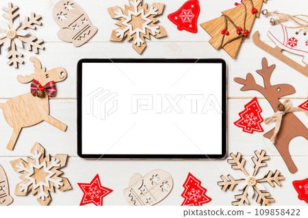 Top view of tablet on holiday wooden background. New Year decorations and toys. Christmas concept Top view of tablet on holiday wooden background. New Year decorations and toys. Christmas concept 109858422