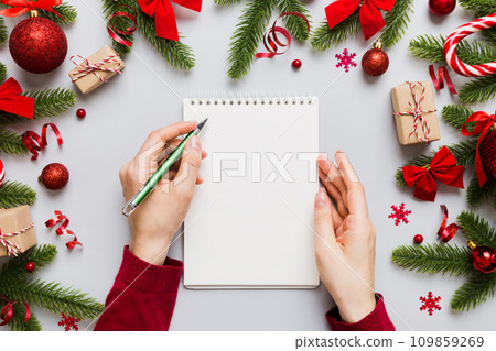Woman writing Christmas to do list on notebook on colored background with xmas decorations Woman writing Christmas to do list on notebook on colored background with xmas decorations 109859269