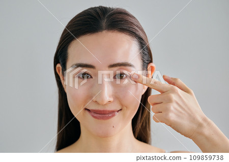 A woman in her 30s putting her finger on her left eye A woman in her 30s putting her finger on her left eye 109859738