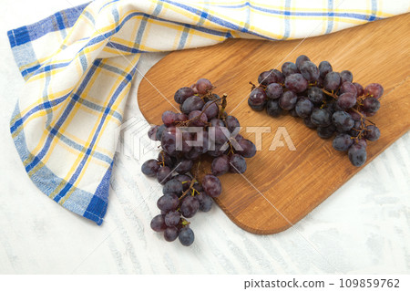 Cutting board with bunch of organic black grapes on white wooden background.. Cutting board with bunch of organic black grapes on white wooden background.. 109859762