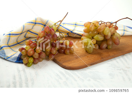Cutting board with bunch of organic pink grapes on white wooden background.. 109859765