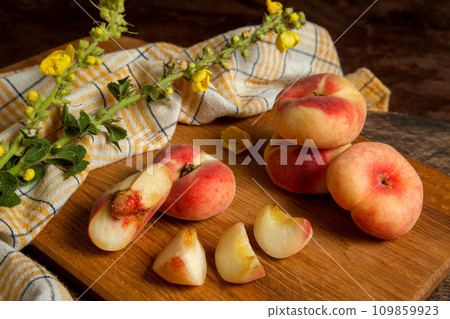 Cutting board with cut and whole saturn peaches or flat peaches on wooden background with yellow kitchen towel.. 109859923