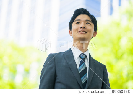 A young businessman walking in a suit among fresh greenery A young businessman walking in a suit among fresh greenery 109860138
