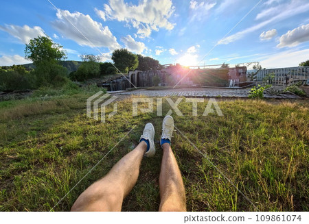 Male feet in white sneakers lying on green grass against background of waterfall closeup Male feet in white sneakers lying on green grass against background of waterfall closeup 109861074