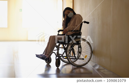 Young disabled woman in protective medical mask sitting in wheelchair in hospital corridor Young disabled woman in protective medical mask sitting in wheelchair in hospital corridor 109861079