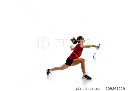 Dynamic portrait capturing athleticism of young, attractive female badminton player in motion during training against pristine white background. 109861229